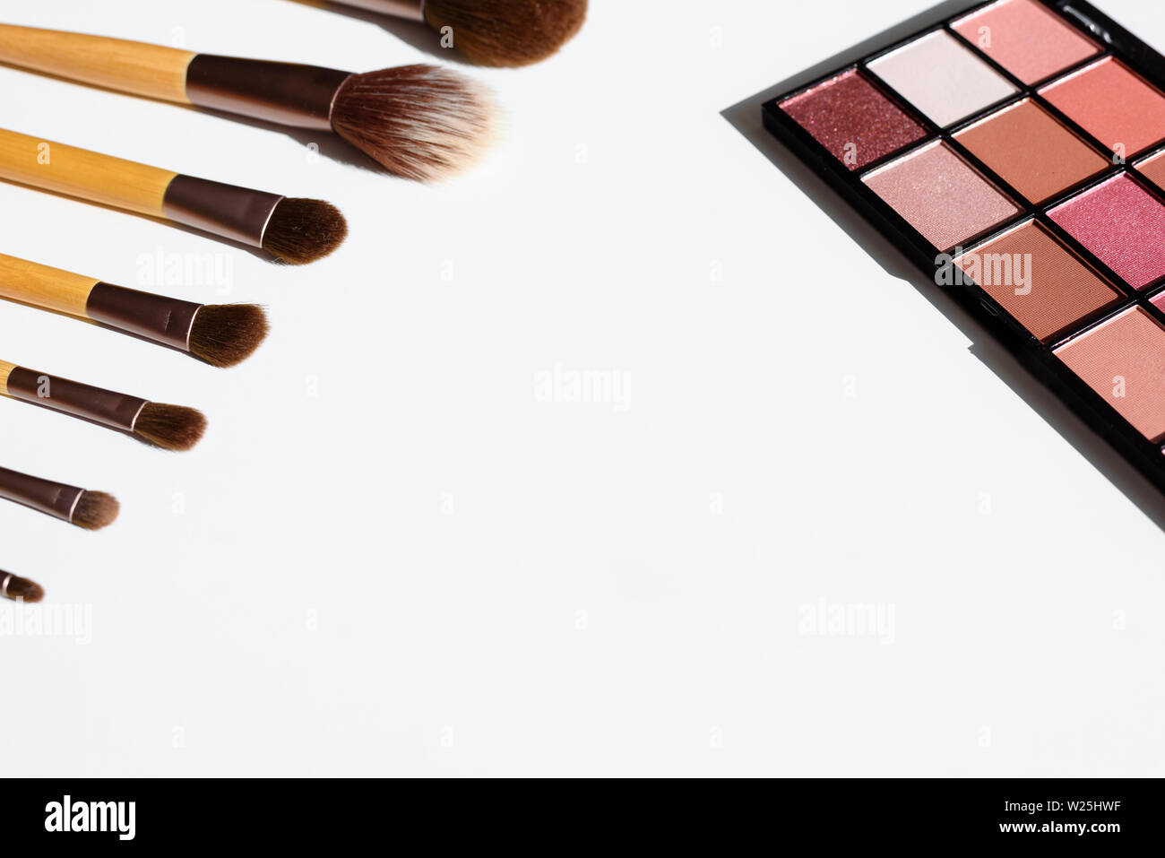 Collezione di make up spazzole disposte in linea, con impugnature in legno. Eye shadow palette in rosa rosso colori. Sfondo bianco con copia spazio. Foto Stock