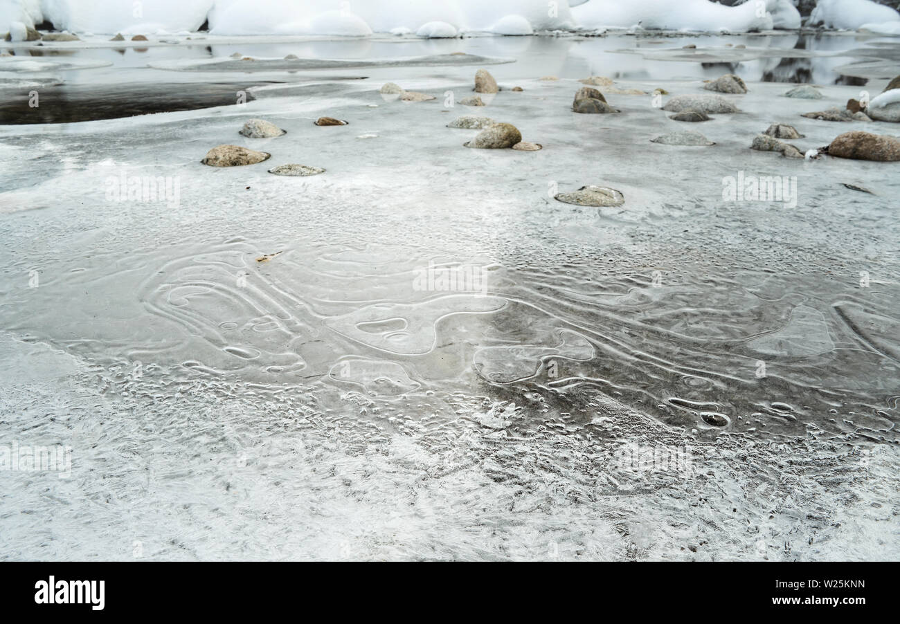 Vista dettagliata del ghiaccio sottile e cristallino di strato di neve sul fiume congelato in inverno, angolo basso foto, ellittica modelli di ghiaccio ed acqua che scorre sotto le pietre, in Foto Stock