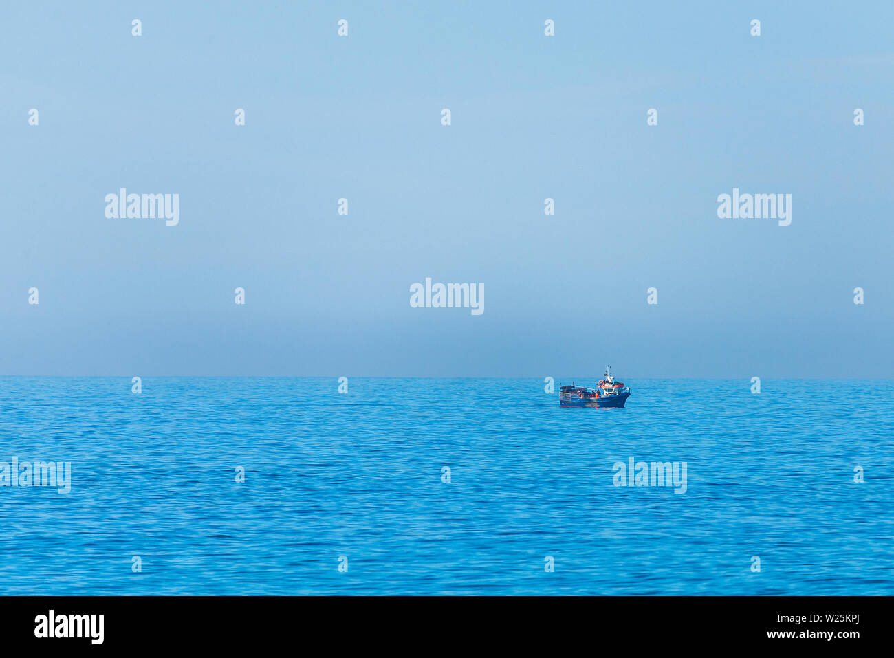 Immagine minimalista sul mare con una barca da pesca. Mare blu acqua e cielo chiaro Foto Stock
