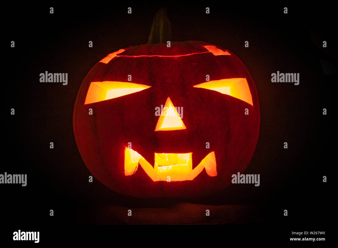 Una grottesca faccia scolpita da Zucca di Halloween con illuminata da una candela accesa all'interno contro uno sfondo scuro Foto Stock