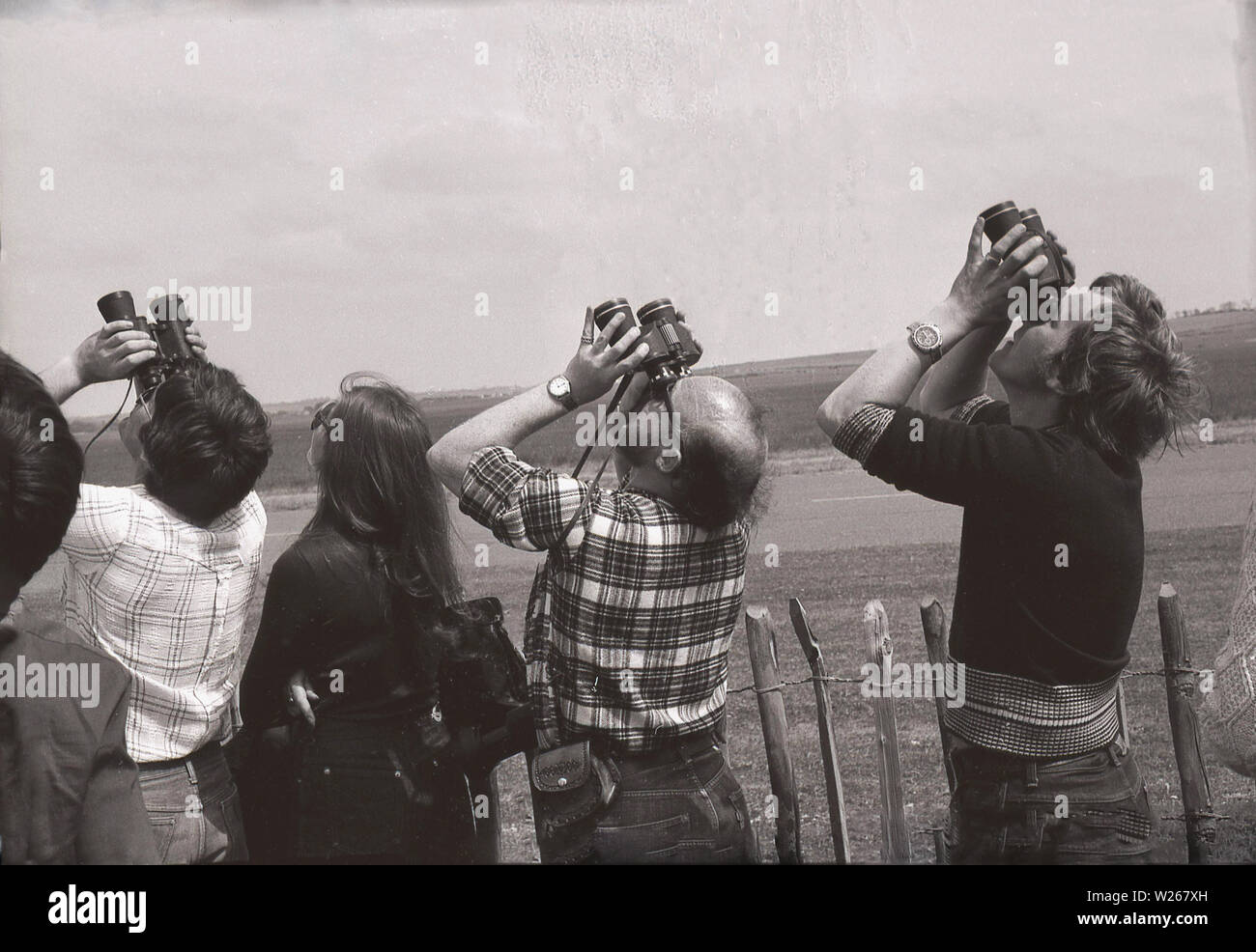 Anni Settanta, storici, gli spettatori in occasione di un'esibizione aerea in piedi dietro una recinzione e utilizzando un binocolo per cercare di distanza, Old Warden Aerodrome, Biggleswade, Inghilterra, Regno Unito. Foto Stock