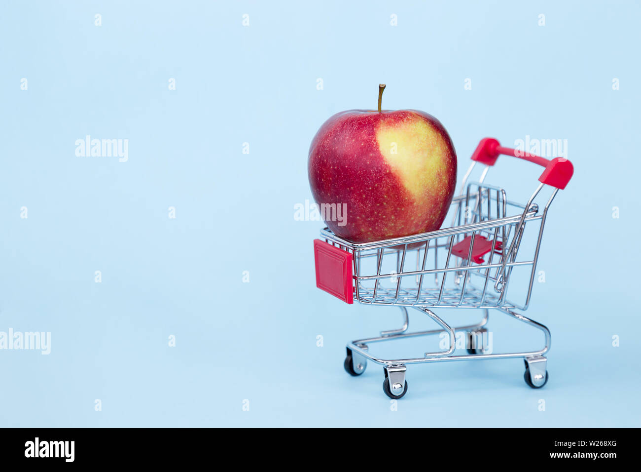 Red apple nel carrello blu su sfondo colorato Foto Stock