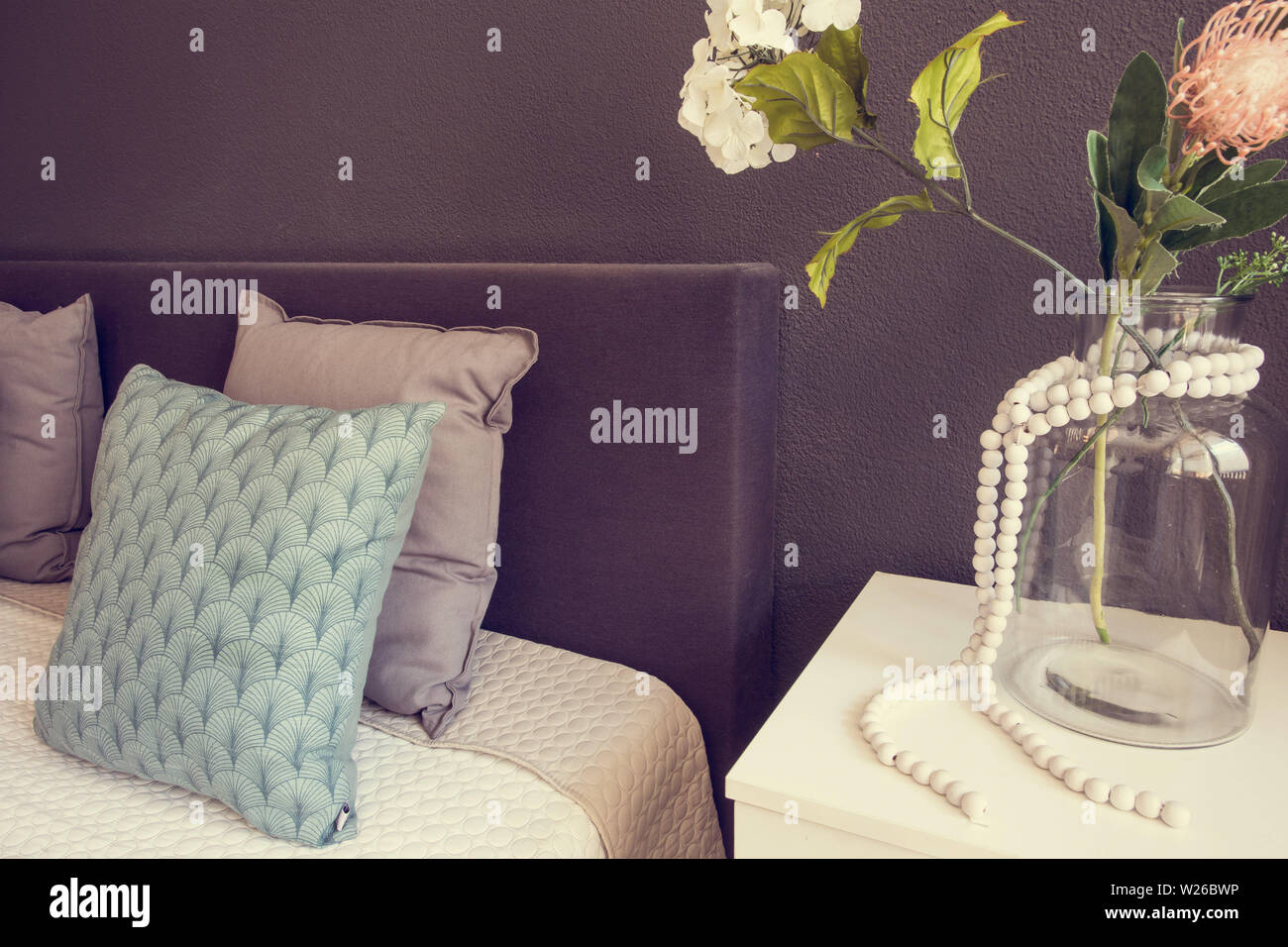 Il letto fatto con pulire i cuscini e le lenzuola nella camera di bellezza. con vaso di vetro e fiori decorativi close-up Foto Stock