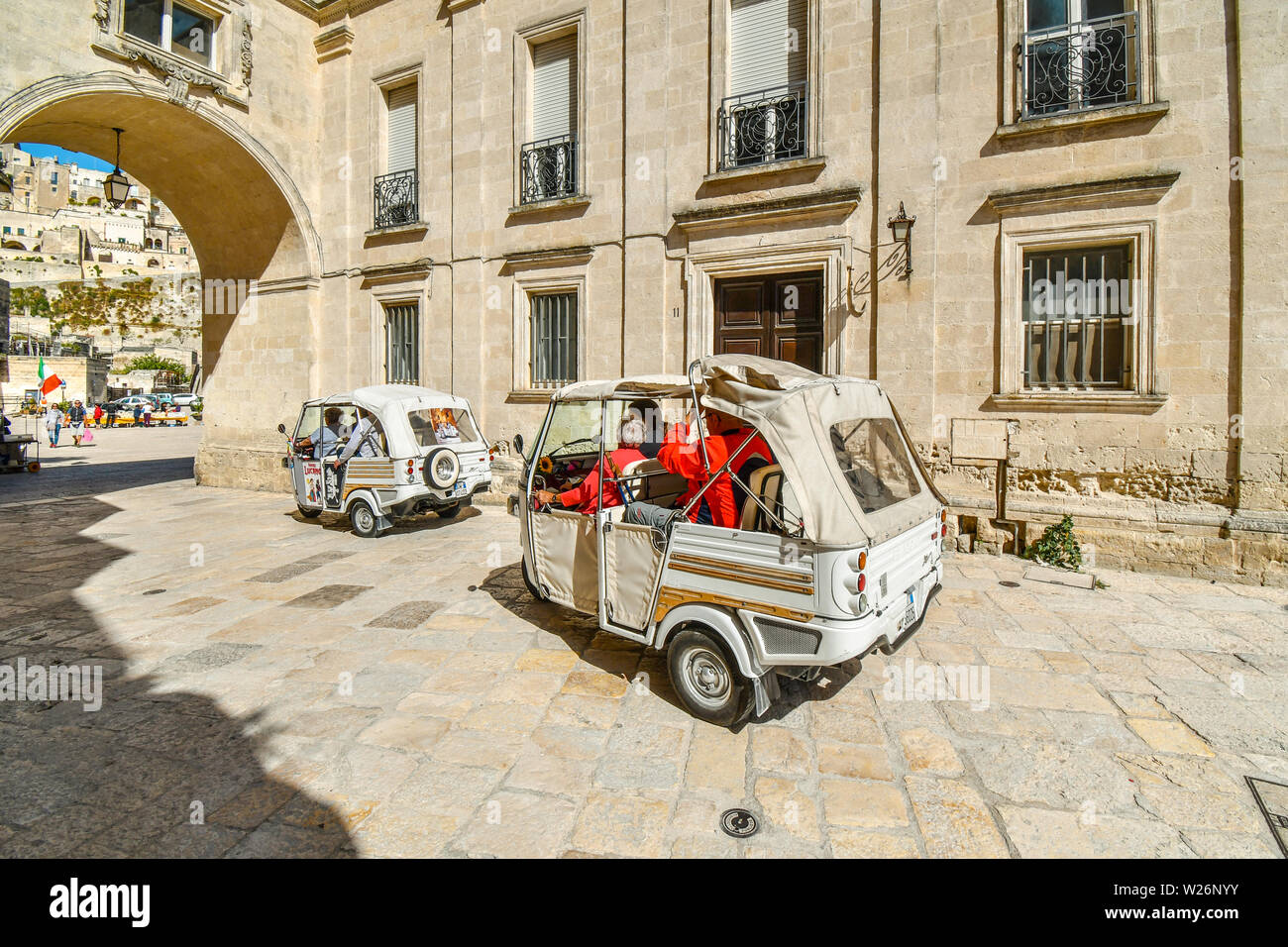 Turisti e guide uso di tre ruote auto per viaggiare attraverso le antiche città di Matera, Italia, un sito Patrimonio Mondiale dell'Unesco. Foto Stock