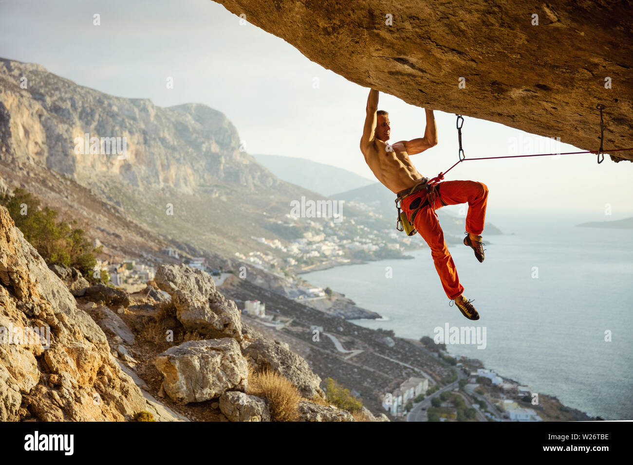 Giovane uomo arrampicata percorso impegnativo in grotta contro la bella vista della costa Foto Stock