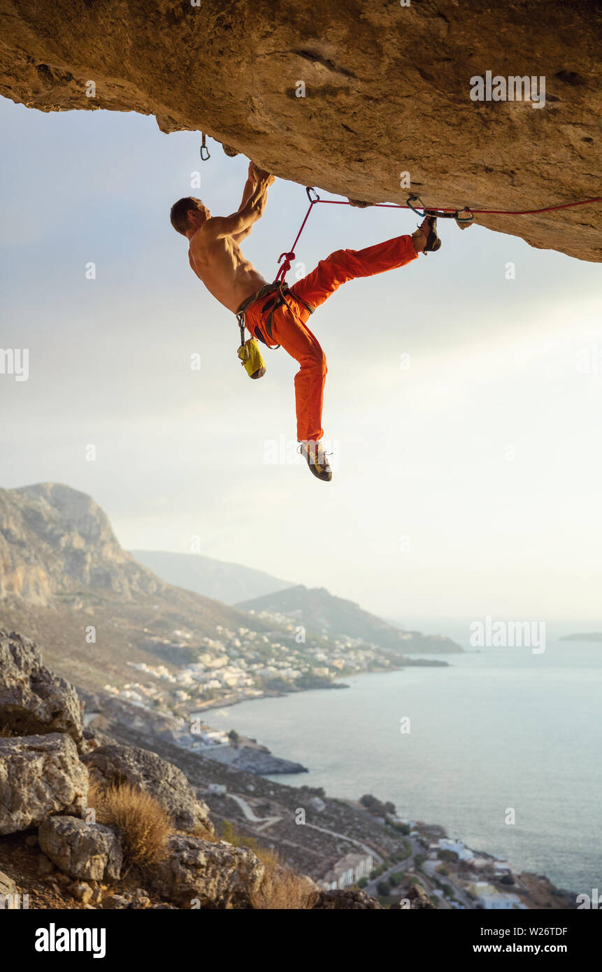 Giovane uomo arrampicata percorso impegnativo in grotta contro la bella vista della costa Foto Stock