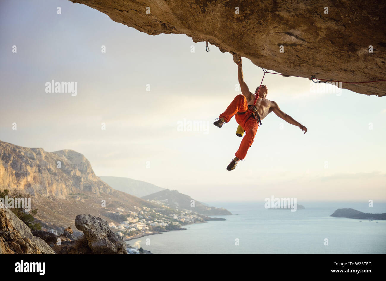 Giovane uomo arrampicata percorso impegnativo in grotta contro la bella vista della costa Foto Stock