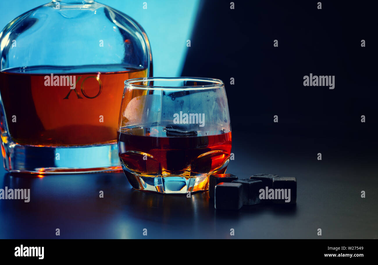 Riutilizzabili cubetti di ghiaccio o nero shungite blocchi di refrigerazione con un bicchiere di whisky di malto e piccole decanter su uno sfondo blu scuro in un pub Foto Stock