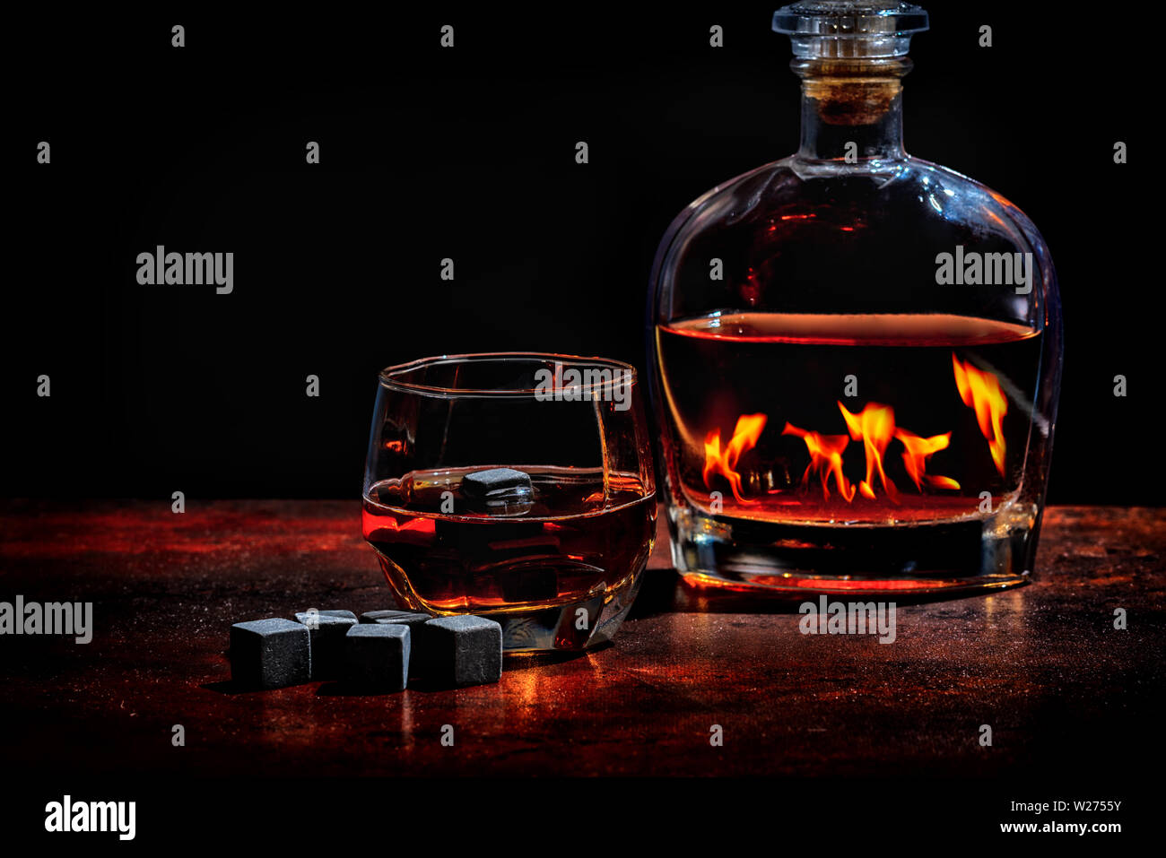 Bottiglia di cognac o di whisky che riflette una fame di un fuoco caldo in inverno con un bicchiere di liquori e riutilizzabili nero di cubetti di ghiaccio o cubetti di refrigerazione Foto Stock