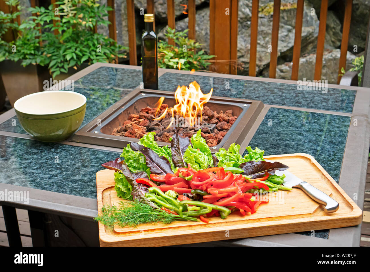 Insalata di fare fuori: peperoni e lattuga sul bordo di taglio sono pronti per essere trasformato in un insalata. Il fuoco sta bruciando per scaldare una fredda giornata. Foto Stock