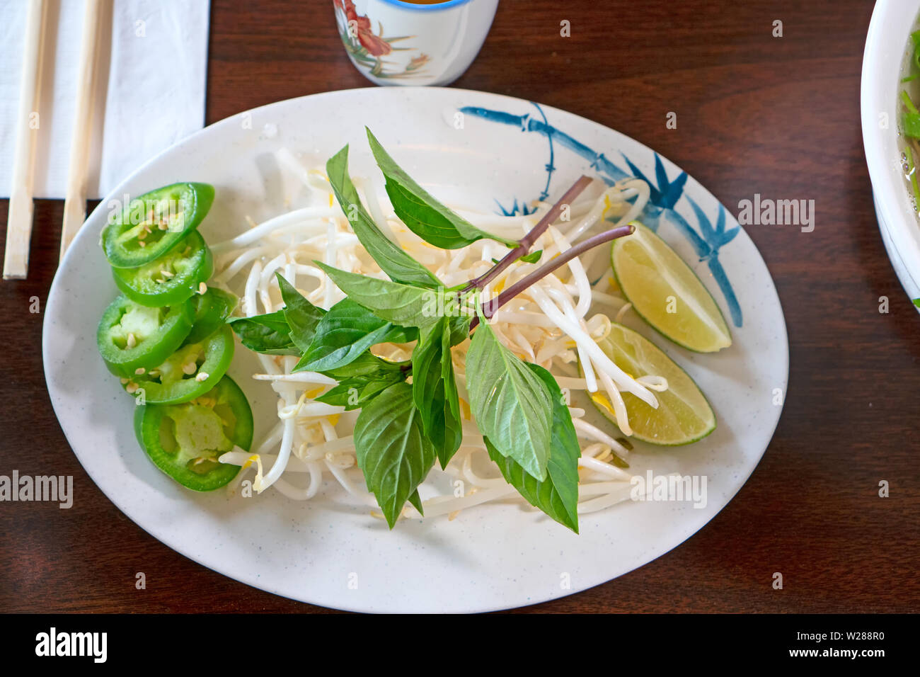 Un piatto con i germogli di soia, jalapeno fette, e basilico - ingredienti servite con la zuppa vietnamita pho. Scatto dall'alto Foto Stock