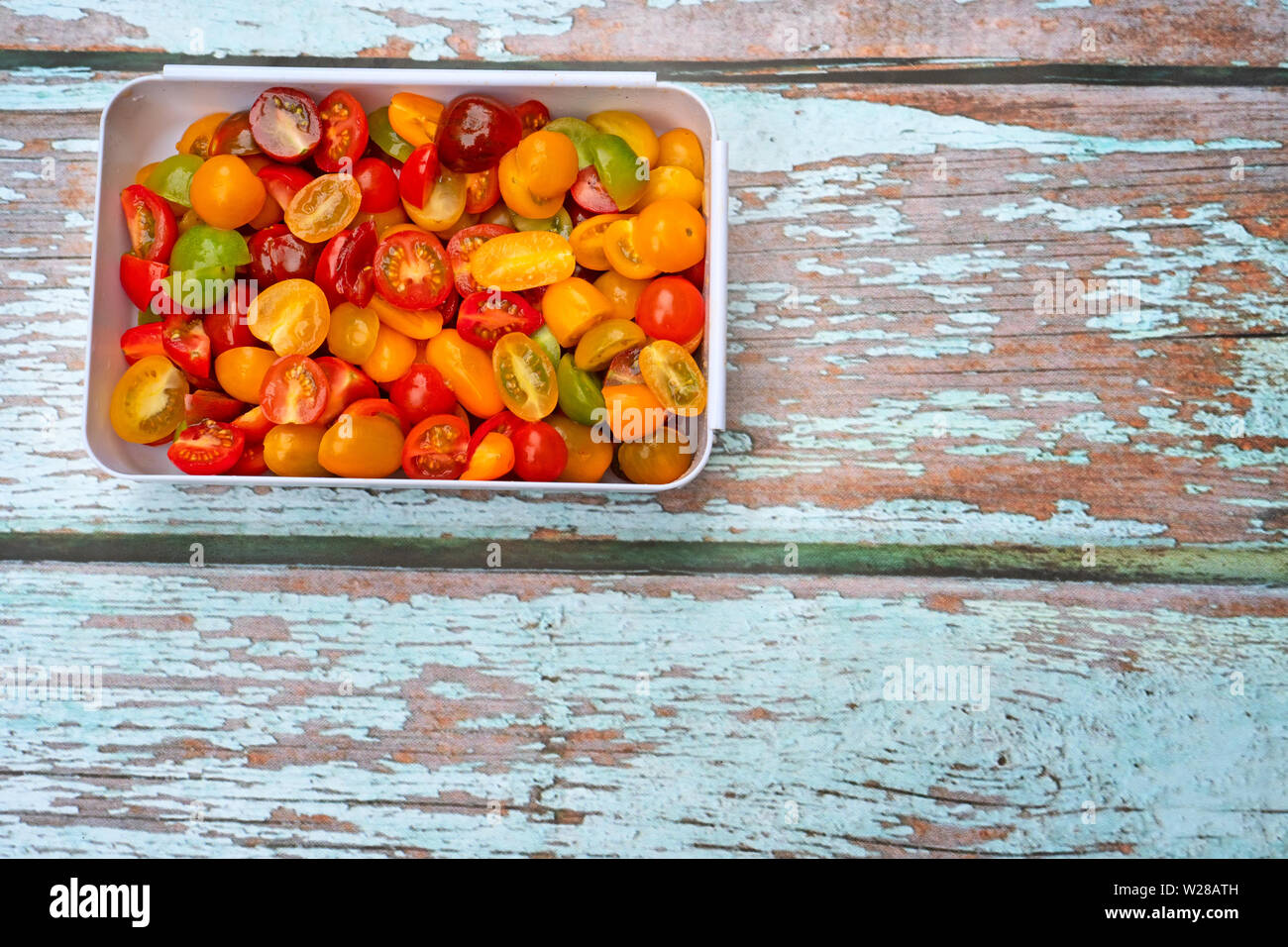 Coloratissimo mix di ciliegia e di mosti di uve i pomodori, tagliate a metà e posto in plastica bianca terrina, su uno sfondo di legno. Foto Stock