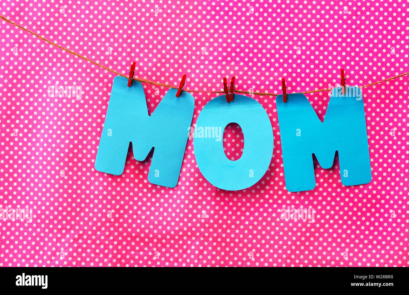 Blue cut-out lettere lettura MOM sono appese con vestiti di rosso i perni con una rosa polka dot sfondo di tessuto Foto Stock
