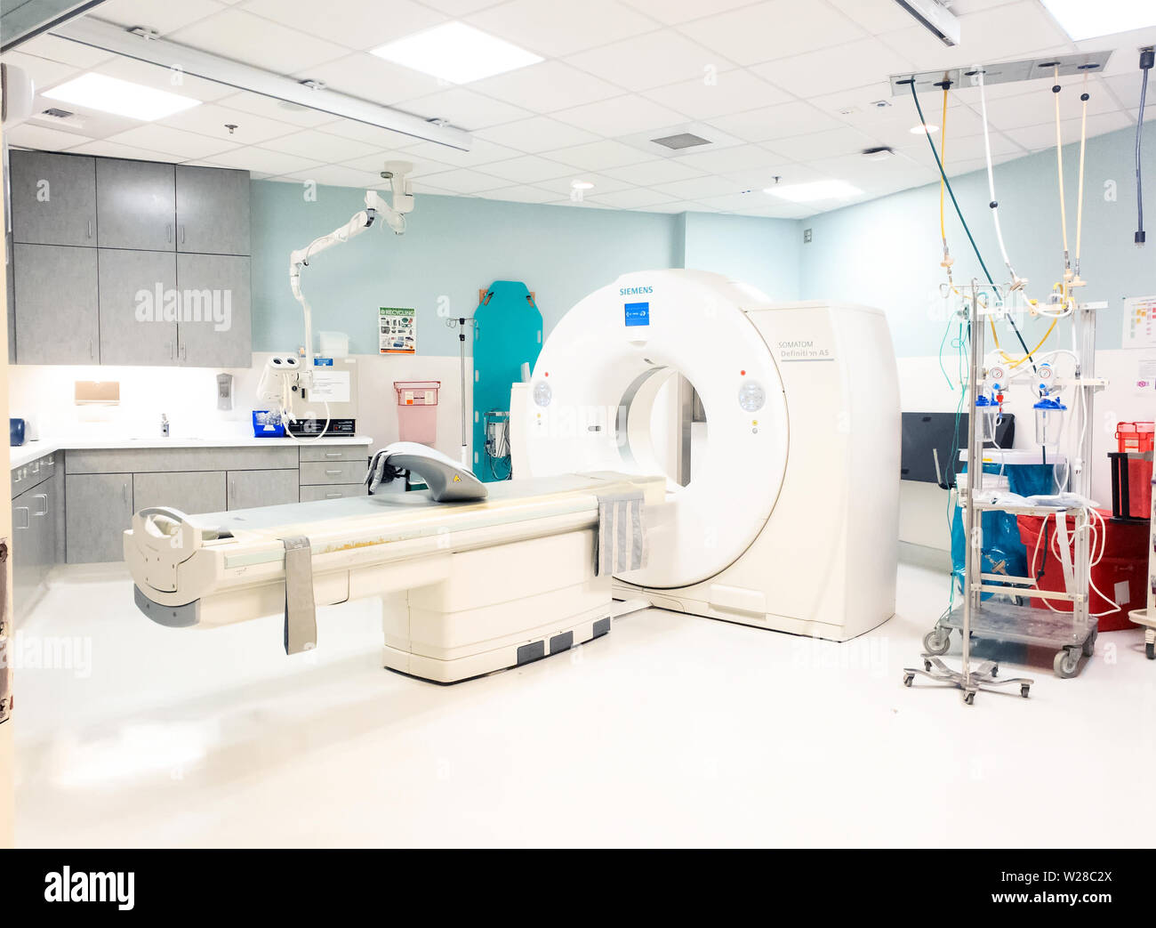 Una macchina Siemens computer Tomography in una suite di radiologia. La tavola spinale appesa alla parete dietro la macchina. Foto Stock