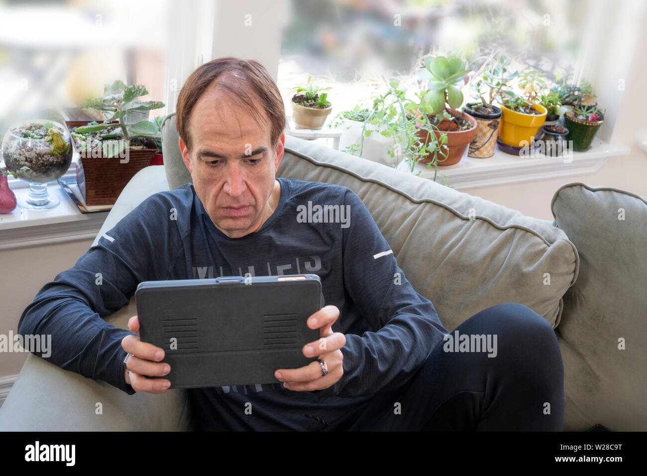 Un uomo di mezza età Per leggere le notizie o i messaggi di posta elettronica su un tablet su un lettino a casa Foto Stock