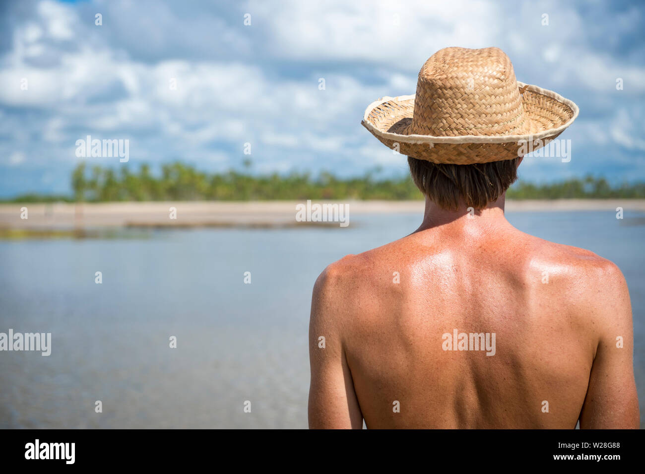 Turismo caucasica indossando una paglia cappello per il sole guardando a una luminosa palme spiaggia Isola di scena, bruciore cutaneo nel caldo sole tropicale Foto Stock