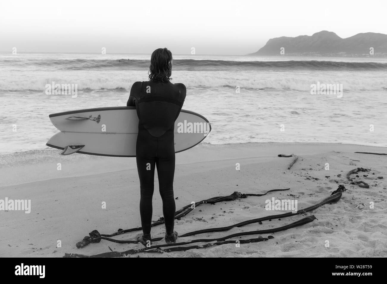 Un surfista a St James sulla spiaggia di pericolo prevede il ritorno in mare durante la visione di un altro insieme di onde in Africa del sud della Penisola del Capo Foto Stock