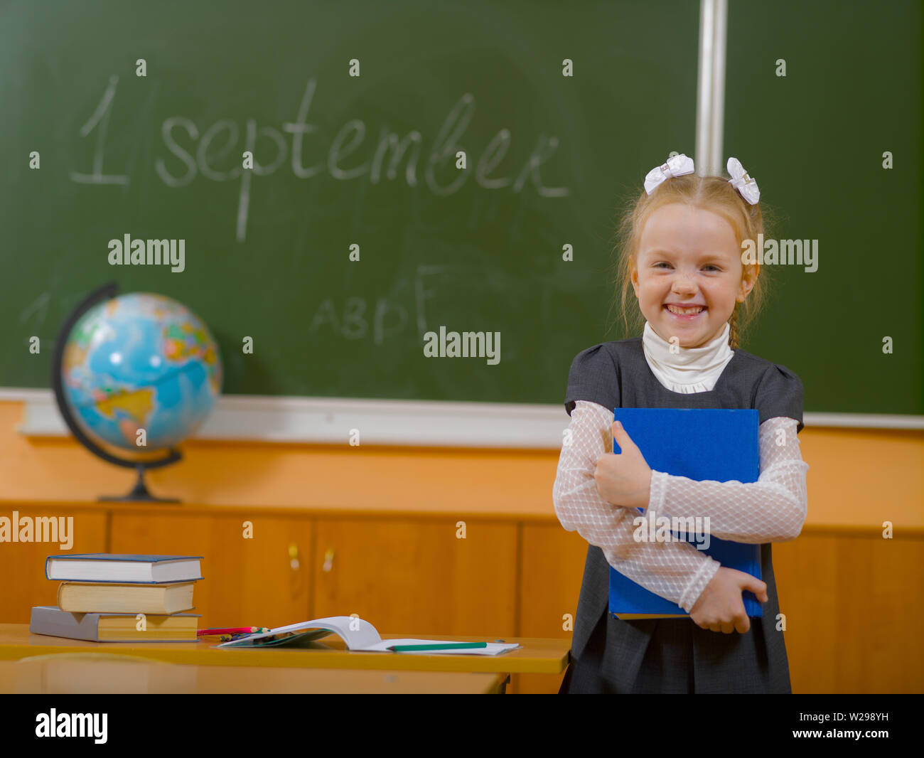 Sorridente schoolgirl è in piedi accanto alla scrivania in aula sullo sfondo del bordo della scuola Foto Stock