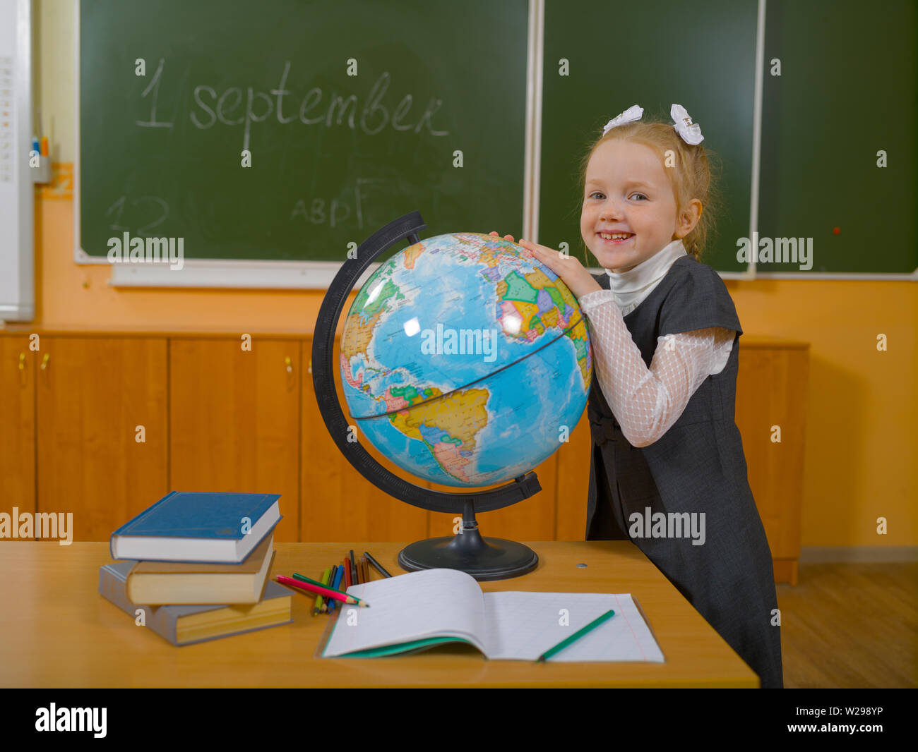La scolaretta sorridente in classe scolastica con globo terrestre contro lo sfondo del bordo della scuola Foto Stock
