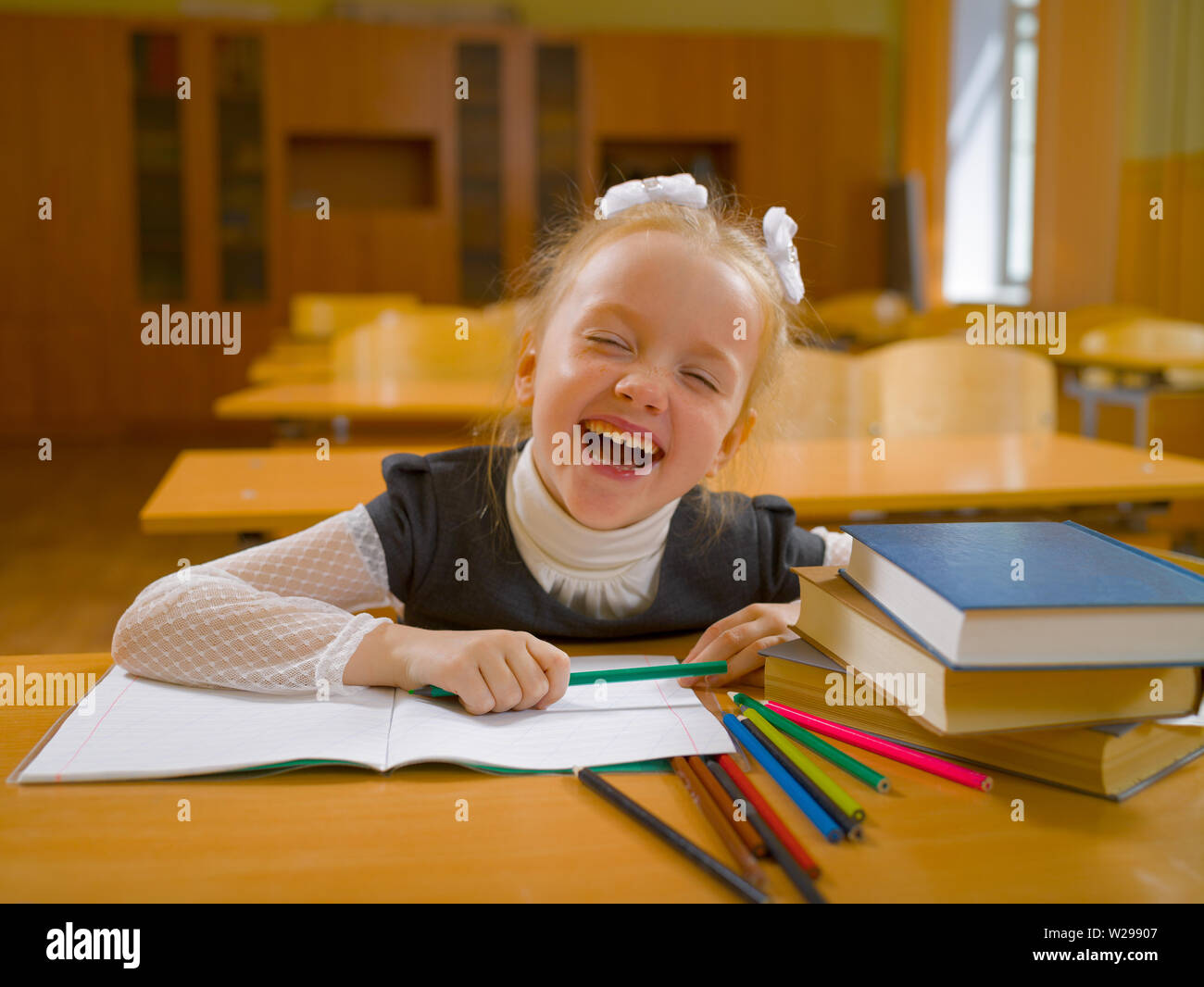 Ridendo schoolgirl siede su un banco di scuola con un notebook, matite e libri in classe Foto Stock