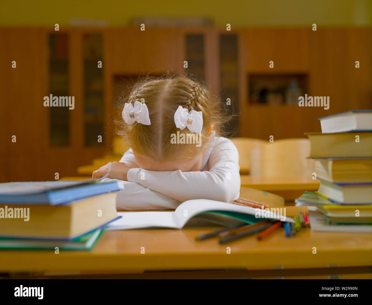 Stanco schoolgirl nella classe scolastica alla lezione alla sua scrivania con un notebook, matite e libri Foto Stock