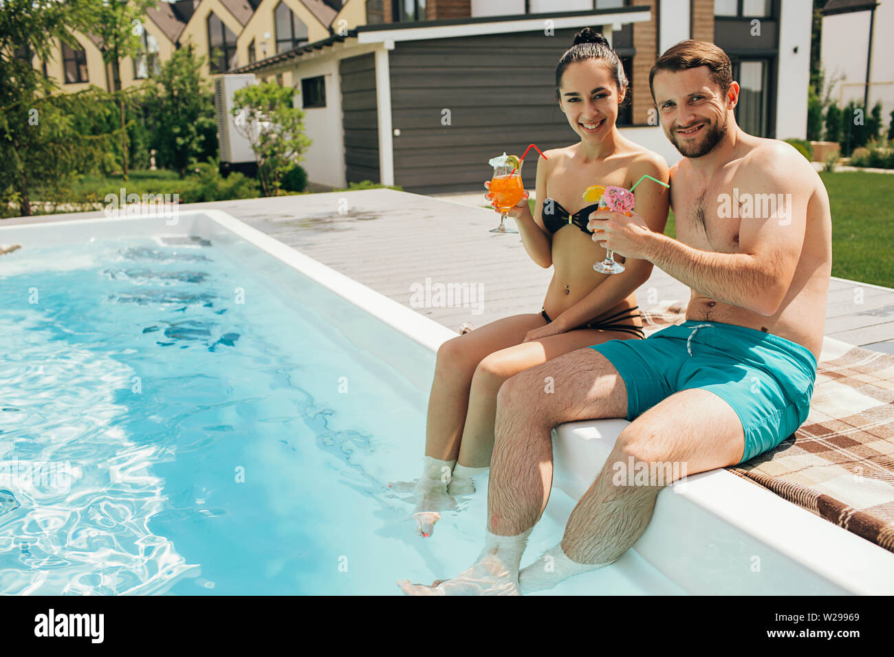 Bella coppia heteroseksual affittato una casa con una piscina. L uomo e la donna seduta vicino alla piscina di acqua e tenendo fresco cocktail Foto Stock