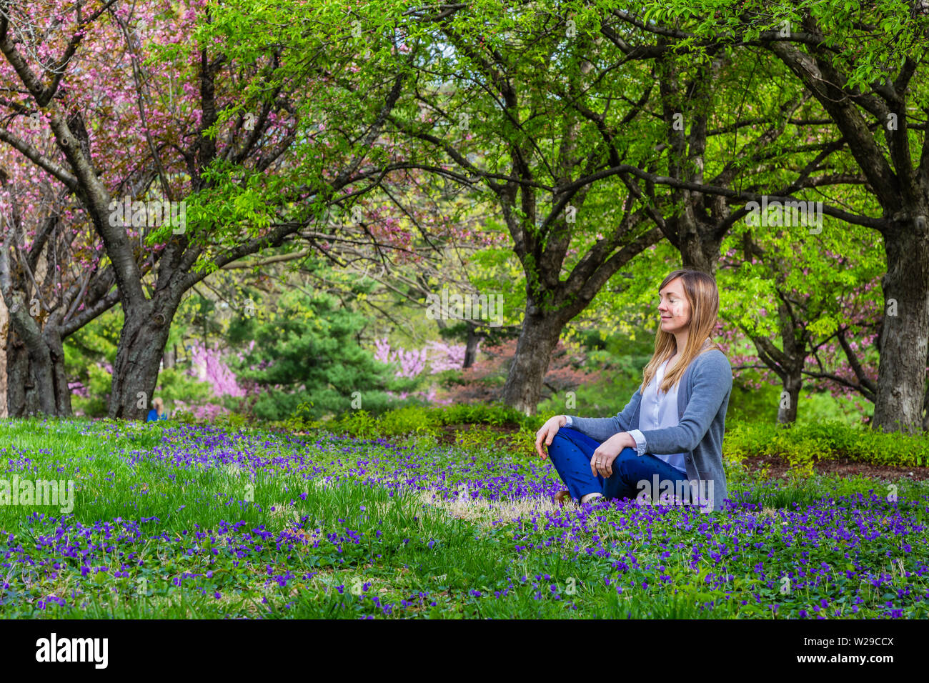 Giovane donna seduta in un parco meditando in una posa di yoga. Foto Stock