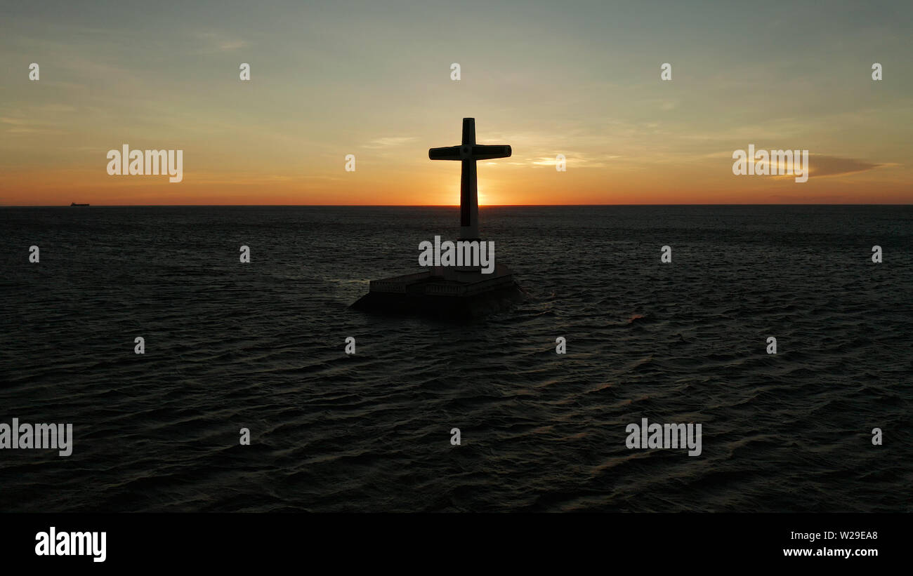 Croce cattolica nel cimitero affondata nel mare al tramonto, Vista aerea. Colorato nubi luminose durante il tramonto sul mare. Tramonto al cimitero affondata Camiguin Island Filippine. Foto Stock