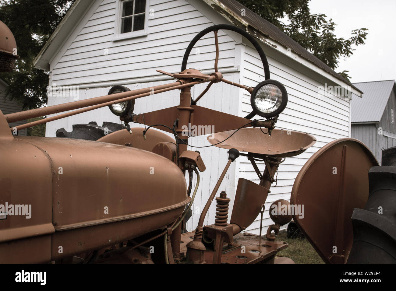 Trattore Antico Rosso Fienile. Trattore antico rosso parcheggiato di fronte a un fienile bianco nel Midwest americano Foto Stock