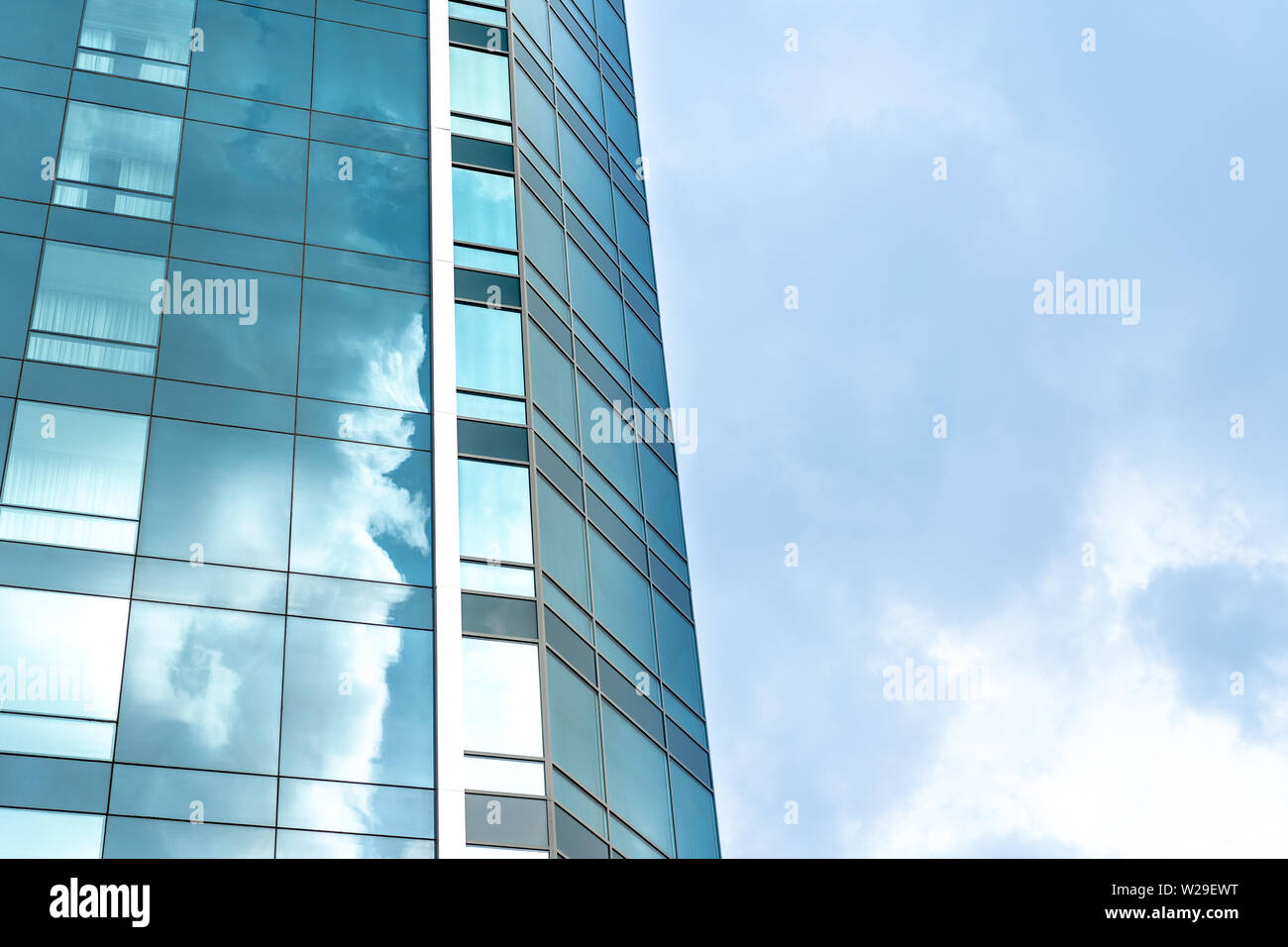 La prospettiva e la parte inferiore dell'angolo di visualizzazione a trama sullo sfondo di un moderno edificio di vetro grattacieli con cielo molto nuvoloso Foto Stock