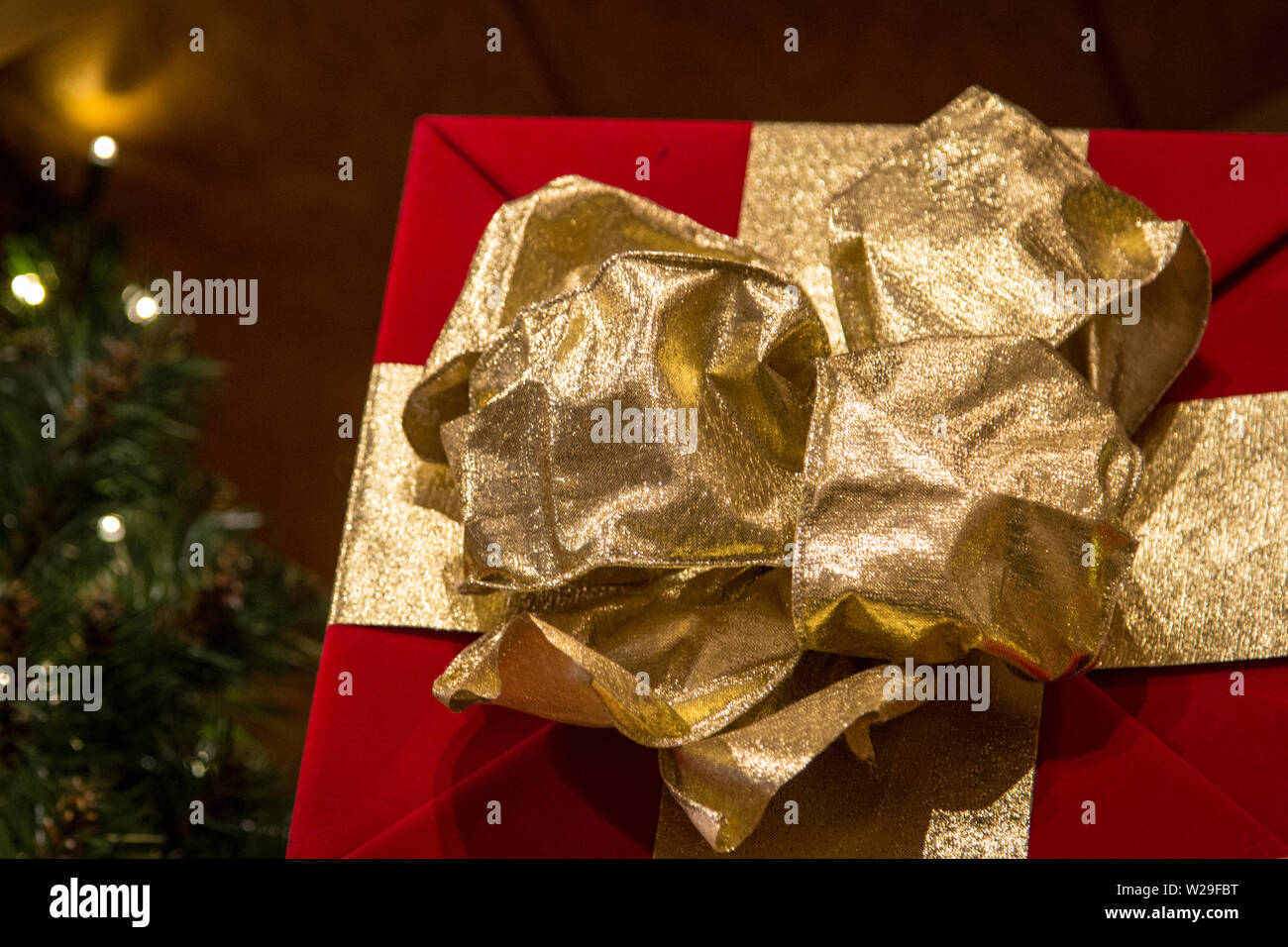 Shopping per il regalo di Natale perfetto. Avvolgere un regalo di Natale con la carta rossa e un ornato di prua in oro bianco con le luci di Natale in background Foto Stock