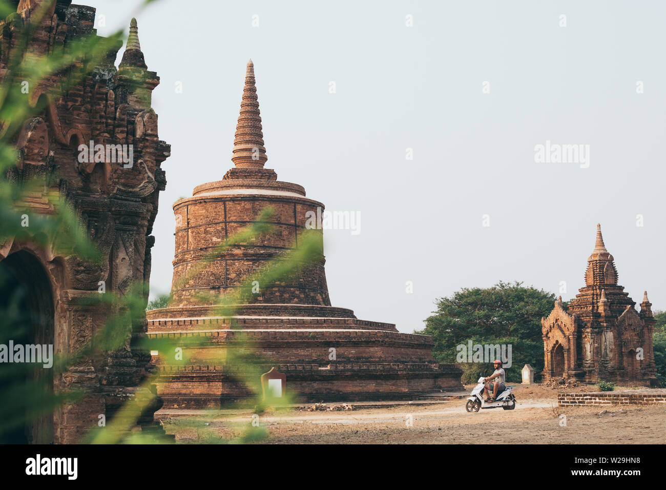 Uomo che cavalca scooter elettrico verso i templi e pagode di antica Bagan in Myanmar. Foto Stock