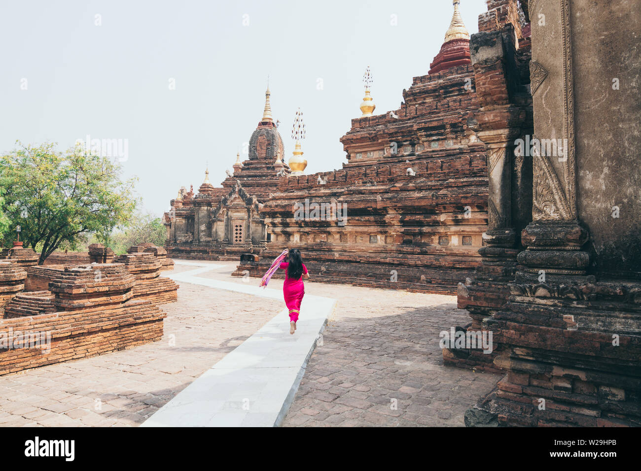 Donna in abito rosso corre vicino al tempio buddista di Bagan, Myanmar. Foto Stock