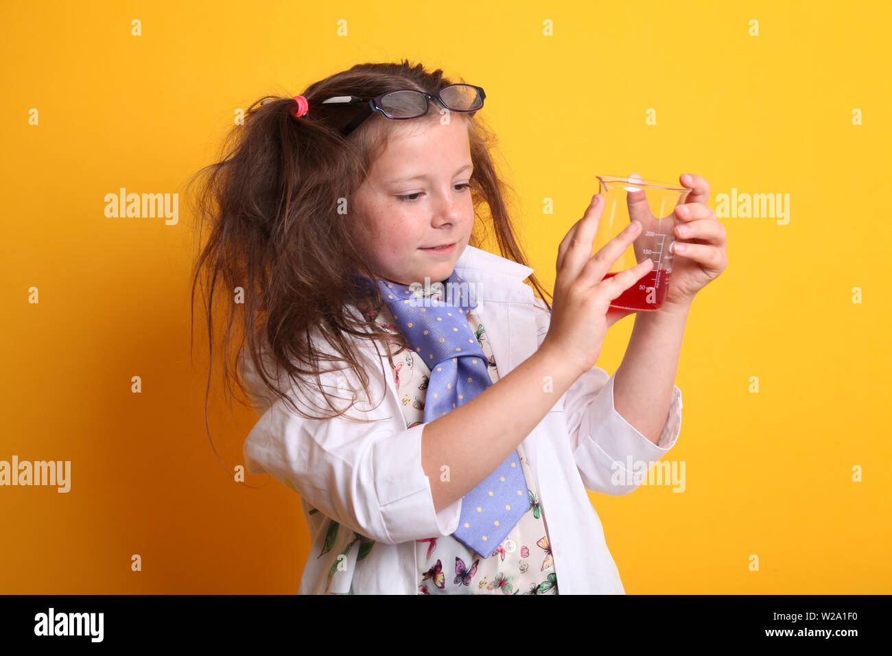 Signor - Scienza Geek giovane ragazza / femmina - 7 anni - bambino misurazione liquido rosso in una scienza di borosilicato becher su sfondo giallo Foto Stock