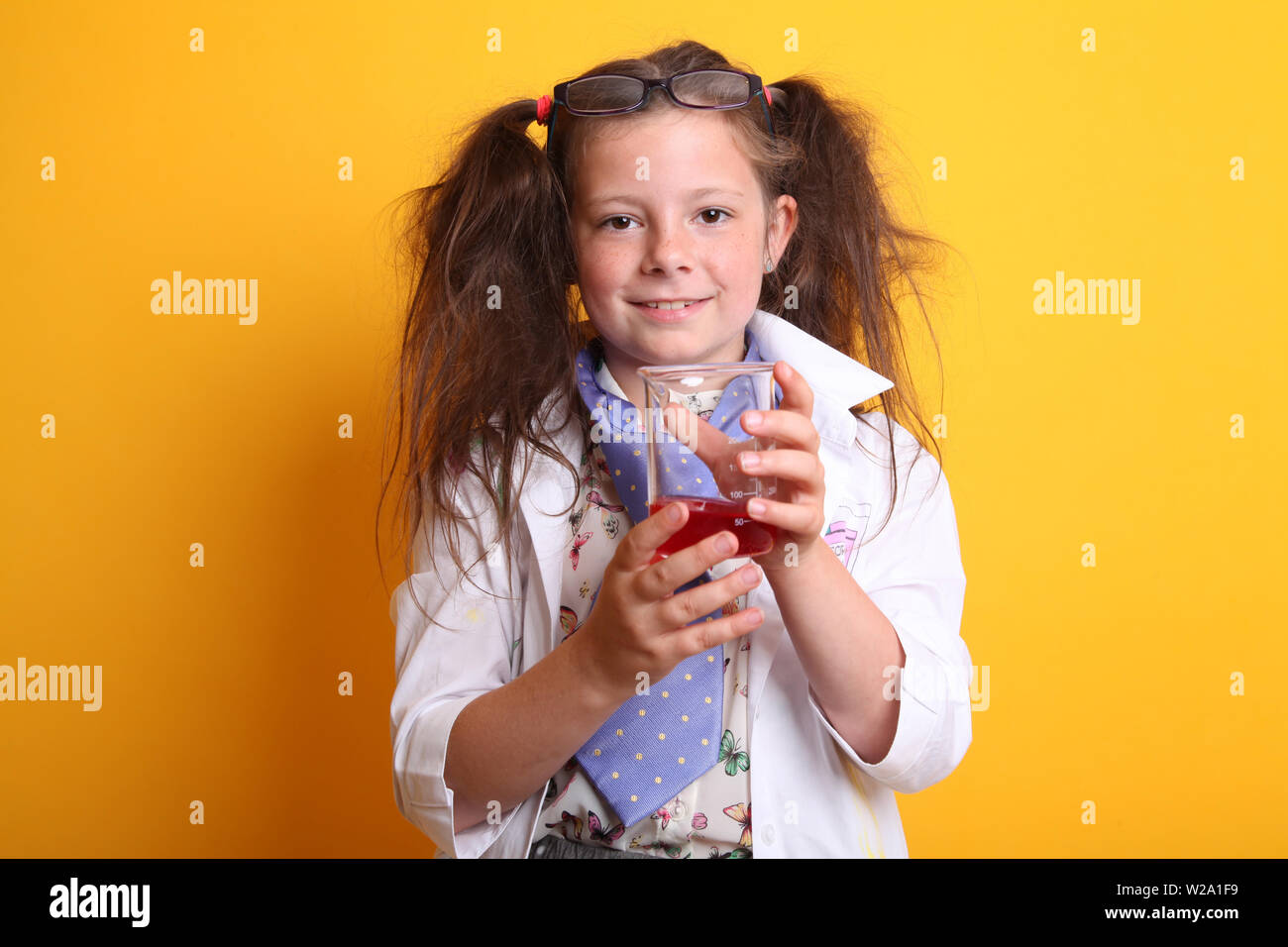 Signor - Scienza Geek giovane ragazza / femmina - 7 anni - bambino sorridente in telecamera tenendo la scienza di borosilicato becher di prodotti chimici di colore rosso su sfondo giallo Foto Stock