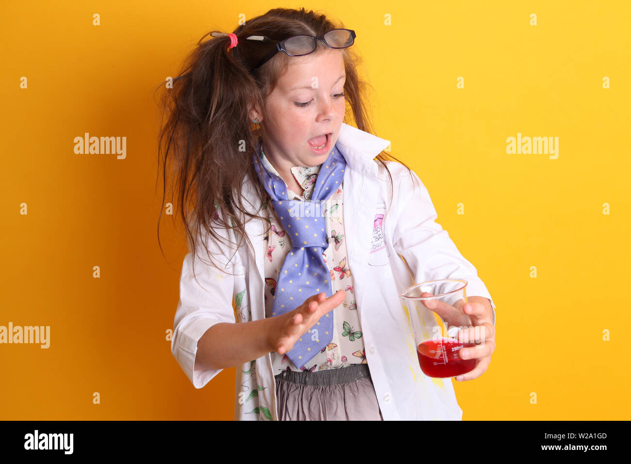 Signor - Scienza Geek giovane ragazza / femmina - 7 anni - bambino guardando sorpreso in borosilicato scienza becher con prodotti chimici di colore rosso su sfondo giallo Foto Stock