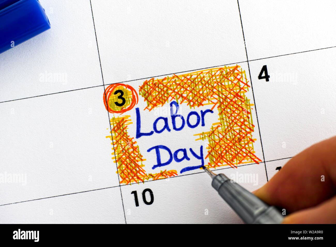 Donna con le dita una penna blu promemoria di scrittura Labor Day in calendario. Close-up. Foto Stock