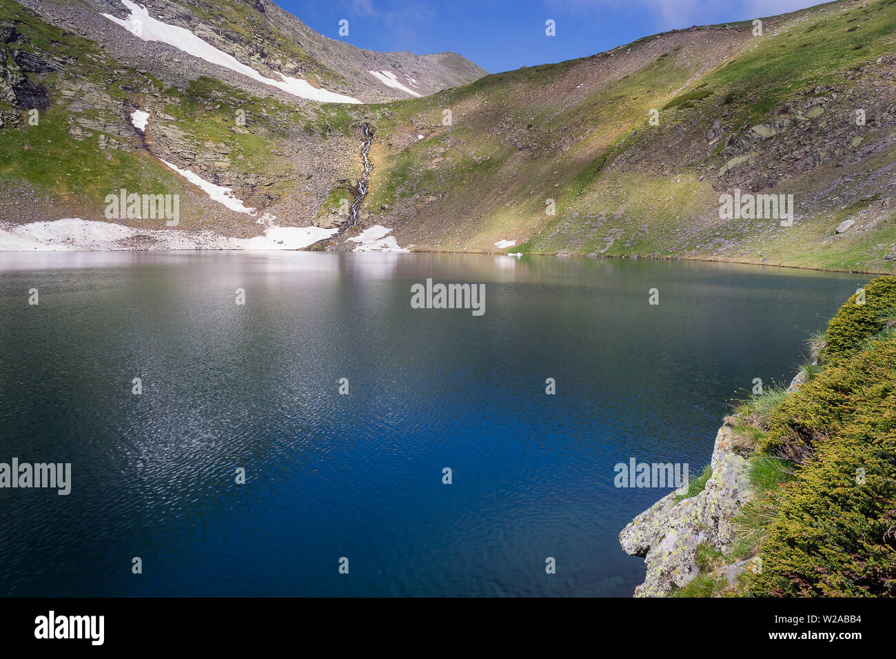 Primo piano soleggiato ginepro, profondo blu del lago gli occhi sulla montagna Rila, scenic cascata a cascata verso il basso la parete rocciosa e vertice distanti Foto Stock