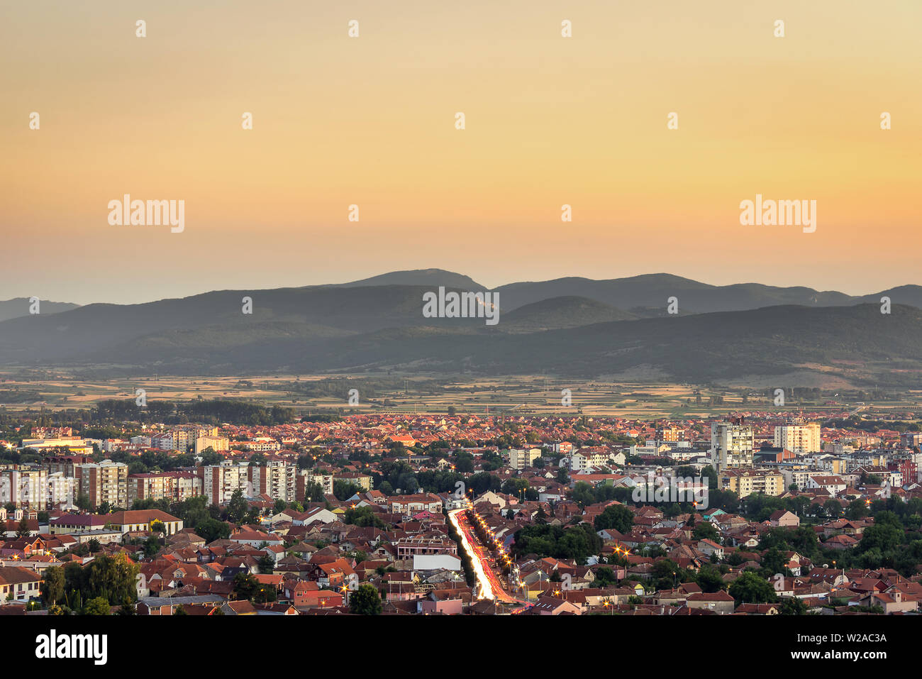 Beautiful golden ora cielo sopra Pirot cityscape con edifici schiarire impostando sun, luci della città e sentieri per auto Foto Stock