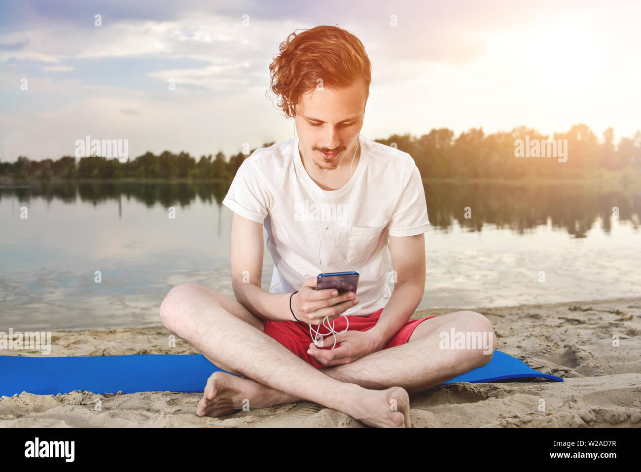 L uomo è seduto sulla spiaggia al lago e la scrittura di un sms sul telefono. buon umore. Bella vista Foto Stock