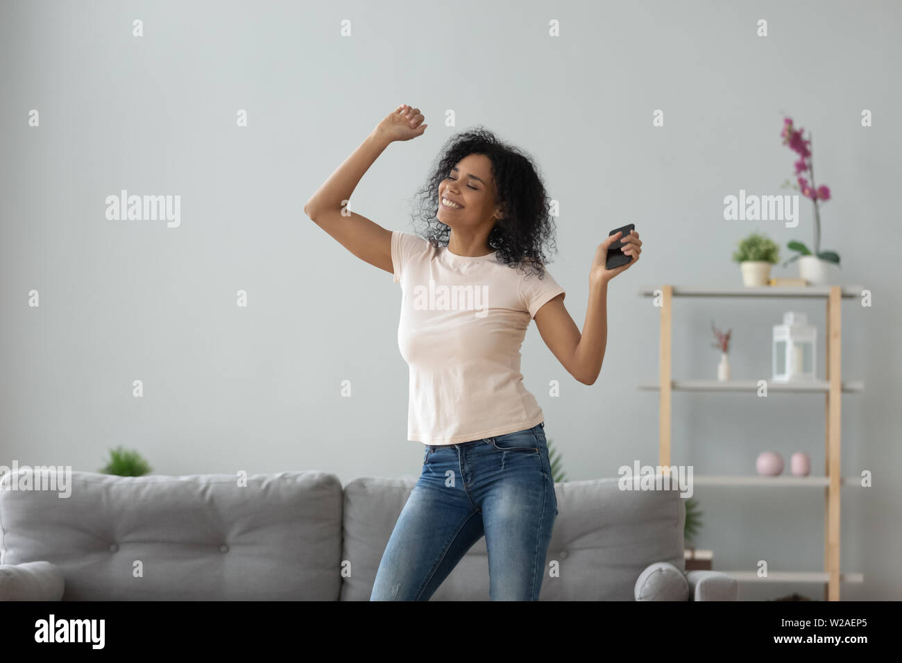 Sorridente active black woman dancing da sola tenendo il telefono in casa Foto Stock