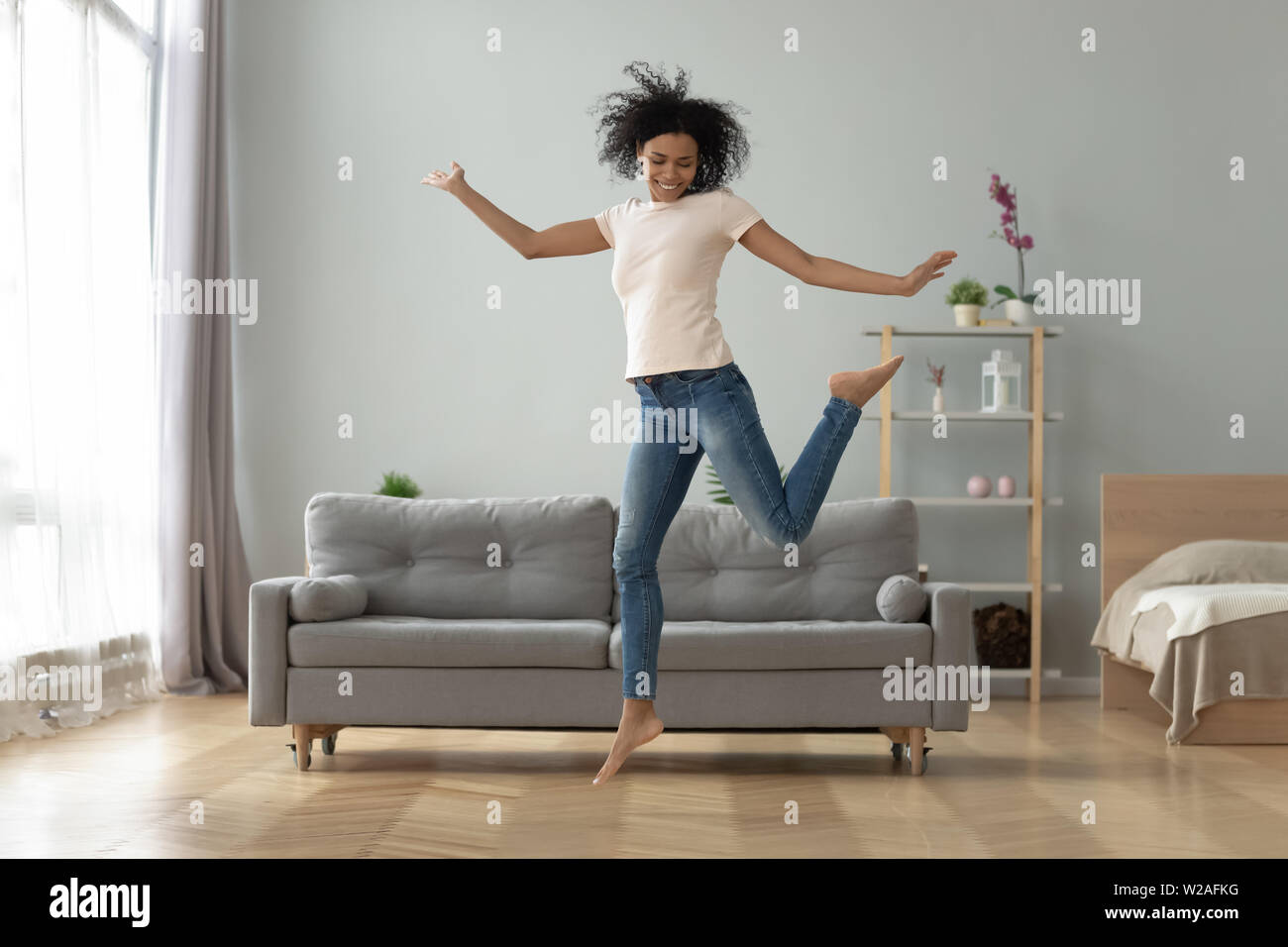 Carefree gioiosa ragazza africana jumping dancing a casa da solo Foto Stock