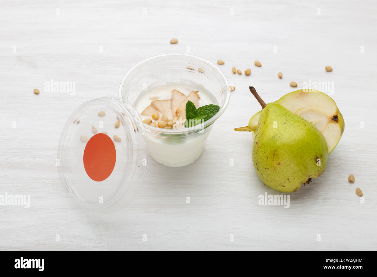 Yogurt fette di pere e menta e pinoli si trovano in una scatola di pranzo su un tavolo bianco accanto a sparse con i pinoli e le fette di pere. Mangiare sano concetto Foto Stock