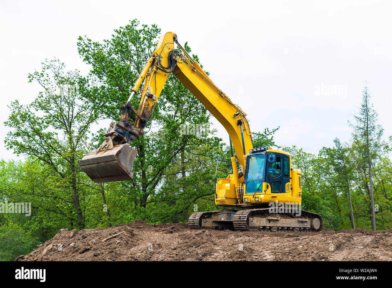 Nastro giallo escavatore sul sito in costruzione. Messa a terra idraulico mover. Il caricatore retroescavatore. Rotazione cabina operatore, pala e traccia continua. Tree Top, sky. Foto Stock