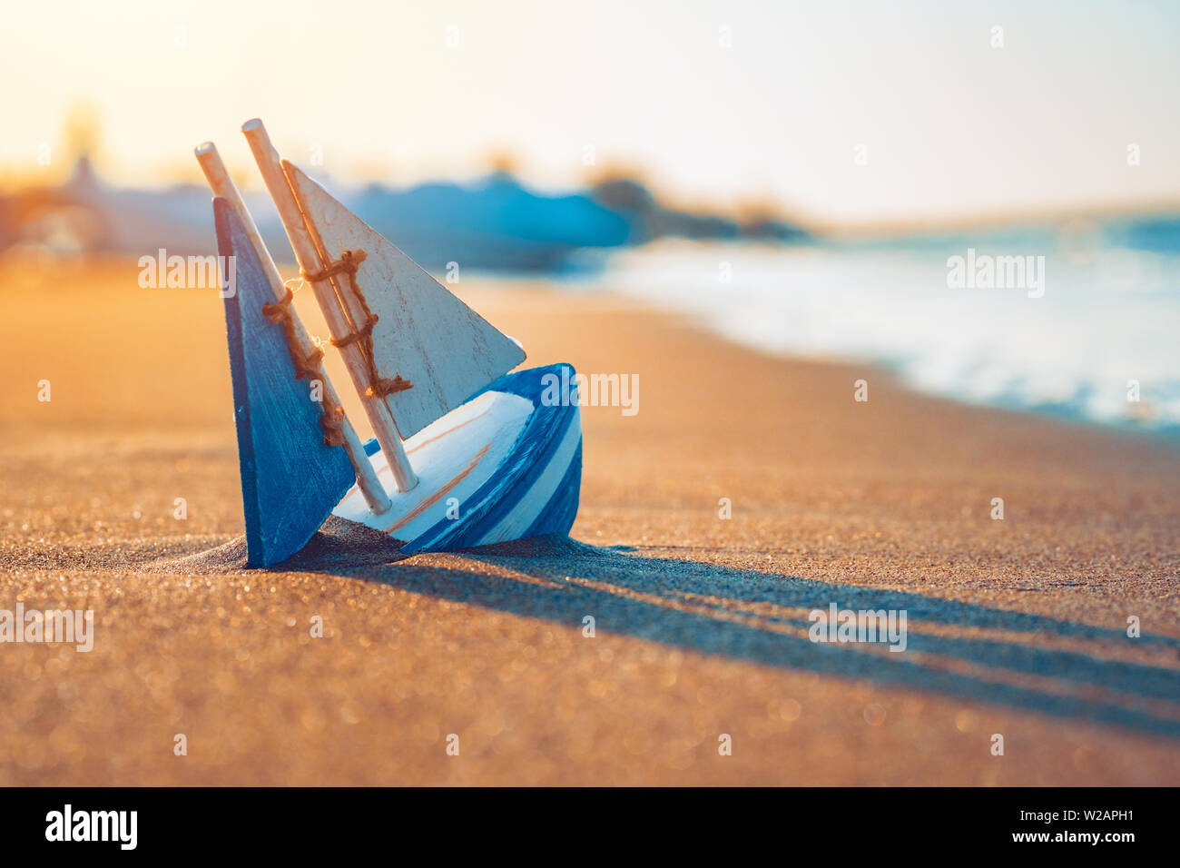 Giocattolo di legno barca a vela sepolto in sabbia vicino la riva del mare in estate. Vacanze e tempo libero concetto concetto. Foto Stock