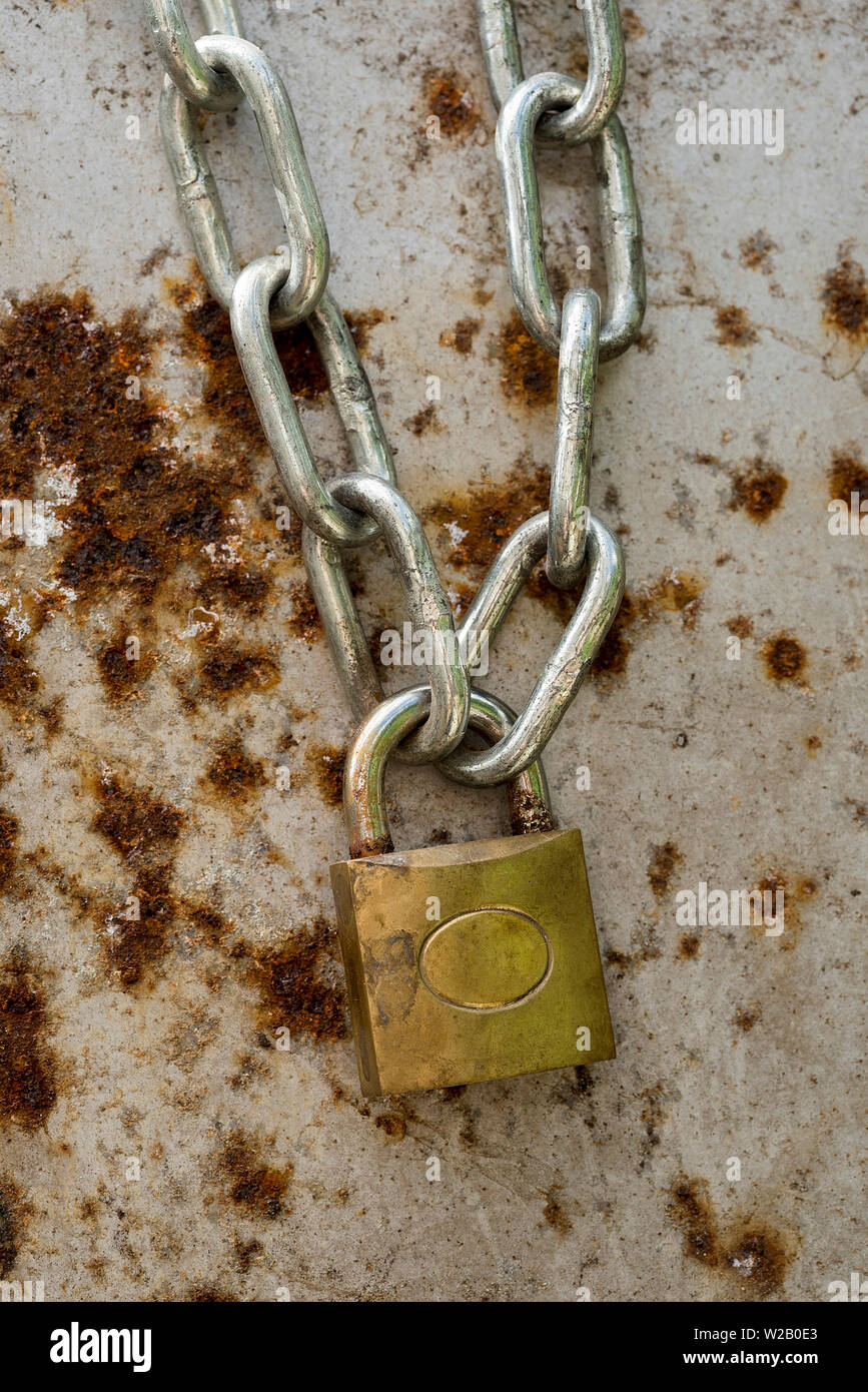 Impieghi leggeri in acciaio e lucchetto in ottone che fissano una catena sulla arrugginendo metallo dello sfondo. Foto Stock