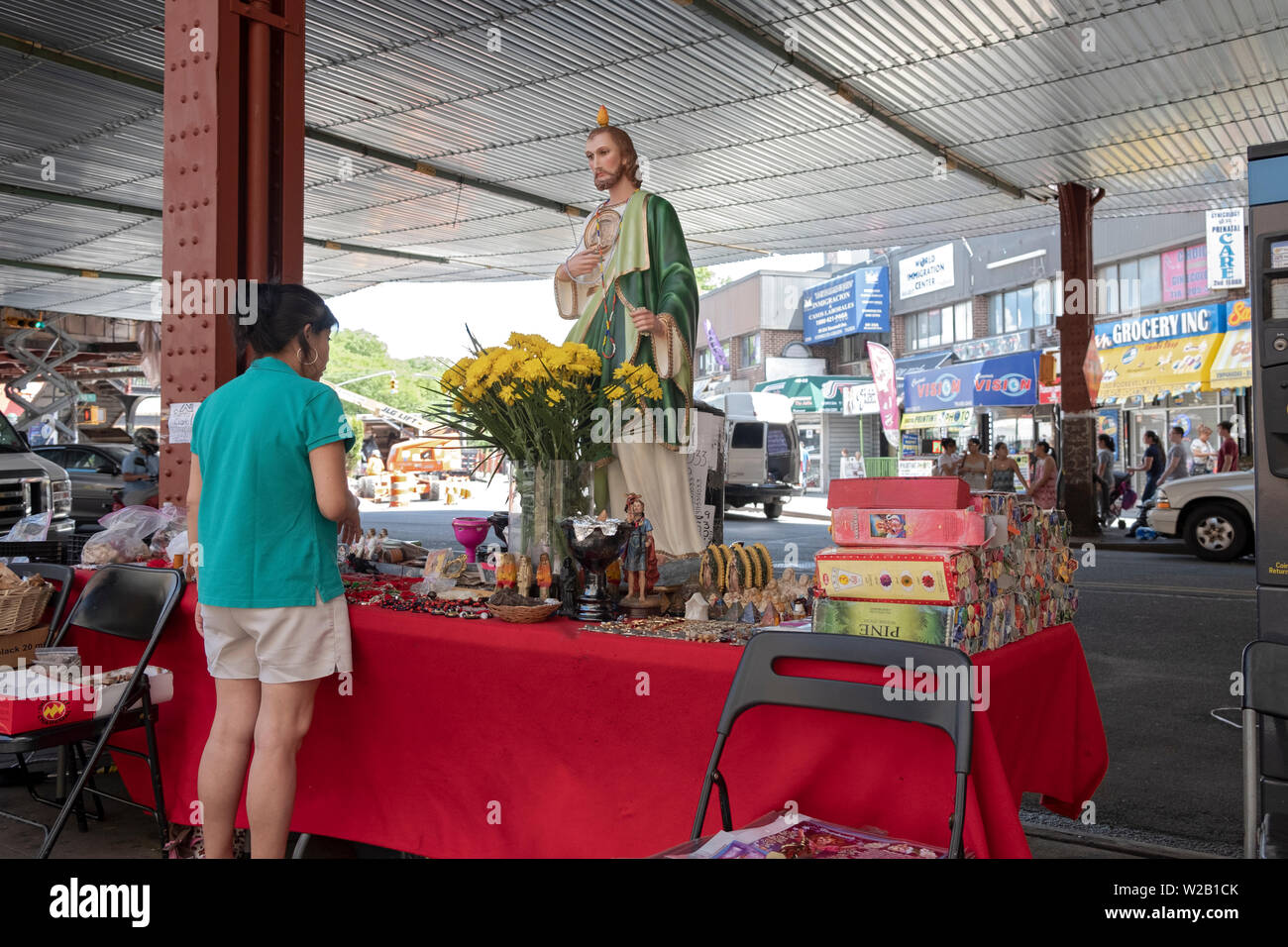 Una donna si ferma a fare acquisti in un stand esterno che vende articoli religiosi. A Roosevelt Ave. sotto la metropolitana sopraelevata in Elmhurst, Queens, a New York. Foto Stock
