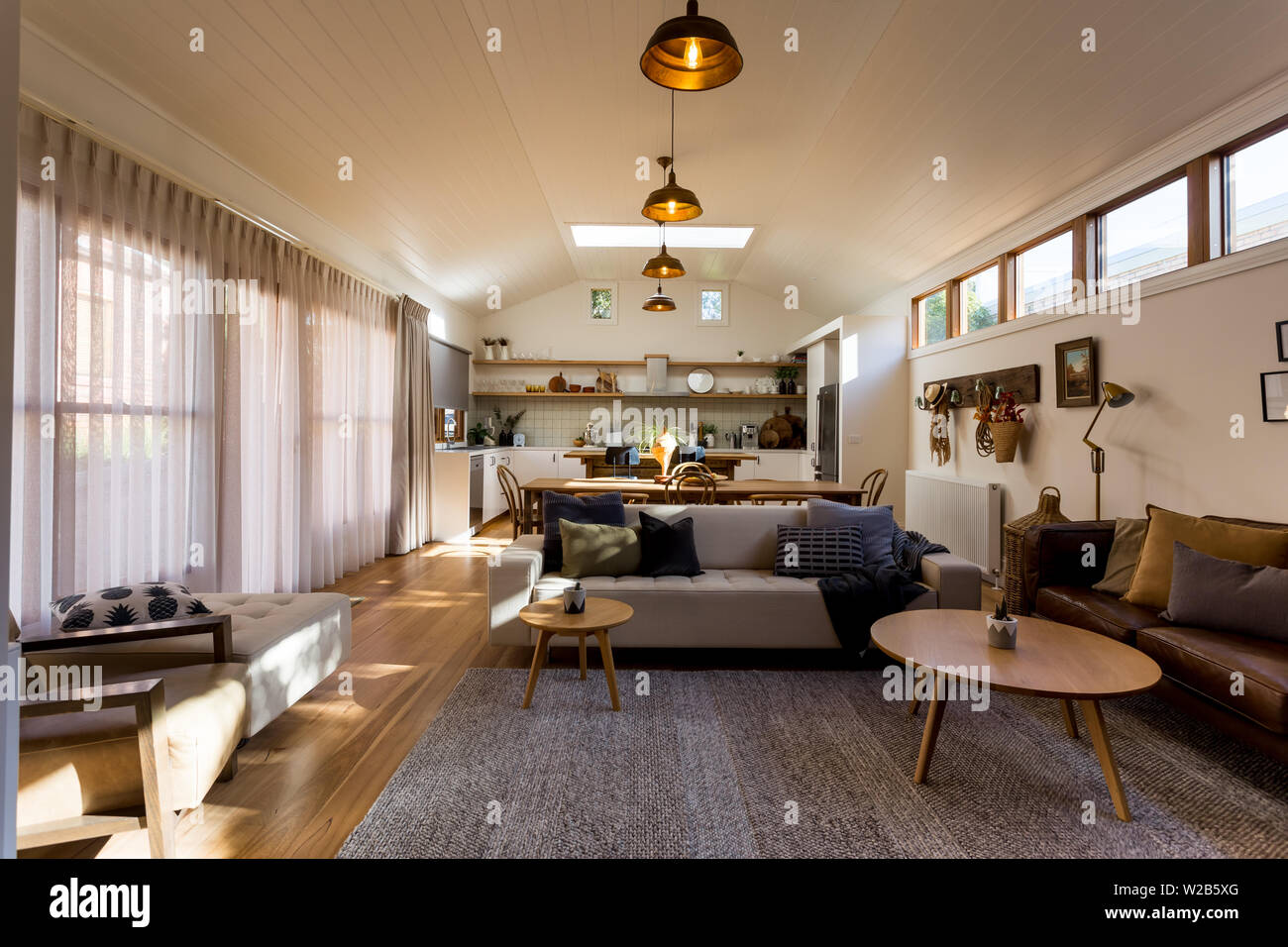 Soggiorno a pianta aperta, cucina e sala da pranzo in una casa di campagna con soffitto soffitto in legno, evidenziare finestre e tendaggi Foto Stock Soggiorno a pianta aperta, cucina e sala da pranzo in una casa di campagna con soffitto soffitto in legno, evidenziare finestre e tendaggi Foto Stock