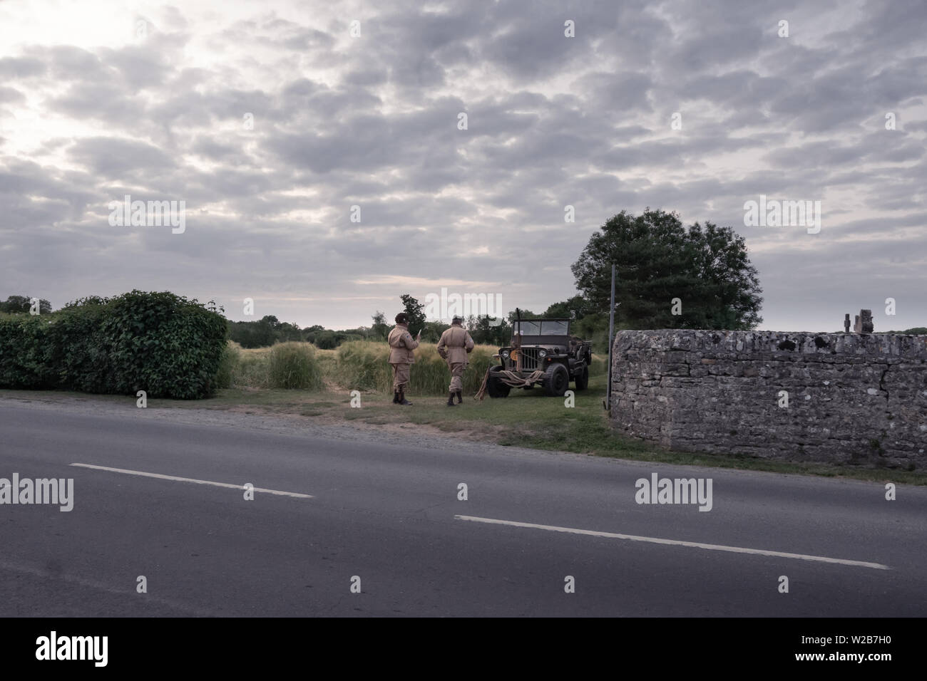 Due uomini vestiti in Guerra Mondiale 2 uniformi nei pressi di un vintage jeep dal lato della strada e la preparazione per una rievocazione storica Foto Stock