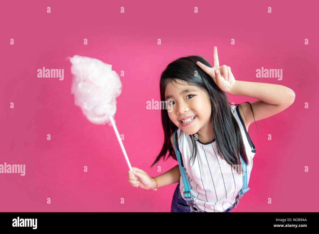 Felice asian capretto bianco mangiare candy cotone su sfondo rosa Foto Stock